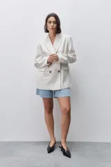Blazer de silueta amplia y largo por debajo de la cadera, color marfil, confeccionado en tela suave y liviana. Presenta cuello con solapas, hombreras, manga larga y cierre cruzado con botones carey.