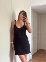 Vestido corto tejido en algodón y lurex, color verde oliva con destellos brillantes. Presenta escote pronunciado en la espalda, breteles con terminación en borlas y diseño calado.