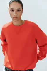 Buzo rojo de cuello redondo y manga larga, con efecto lavado y detalle de costura triangular en el cuello.