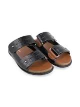 Sandalias de dos tiras anchas en cuero negro con textura de cocodrilo, detalle de remaches metálicos y base de corcho con plantilla marrón.