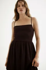 Vestido midi marrón con efecto arrugado, escote cuadrado, breteles finos ajustables y cuerpo elástico en punto smock. Presenta costura fruncida en la cintura y falda con vuelo.