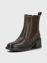 Bota tipo botín de cuero color marrón oscuro, con elásticos laterales y detalles de tachas metálicas doradas a lo largo de la caña. Cuenta con suela gruesa y taco cuadrado de altura media.