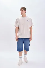 Camiseta manga corta oversize color gris claro con estampa azul en la espalda que incluye texto "Fizz & Tea" y el dibujo de un vaso con hielo.