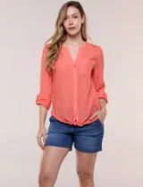 Blusa de calce relajado color salmón, confeccionada en tela liviana con textura sutil. Presenta escote en V con abotonadura frontal, bolsillo parche en el pecho, mangas largas regulables con presilla y ruedo con opción de anudar en el frente.