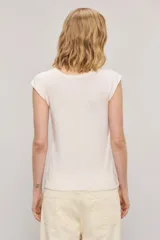 Remera color blanco roto, de calce slim, cuello redondo y manga corta con detalle de hombreras y pequeño bordado en el centro del pecho.
