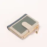 Billetera compacta de tres colores: azul marino, verde grisáceo y beige. Cuenta con un cierre de botón a presión y un bolsillo exterior con cierre de cremallera, adornado con un charm de imperdible dorado y negro.