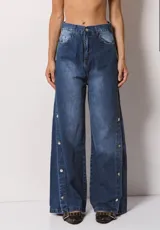 Pantalón de jean azul de corte wide leg, con diseño de botones metálicos a presión a lo largo de las costuras laterales. Presenta un lavado localizado y tiro alto.