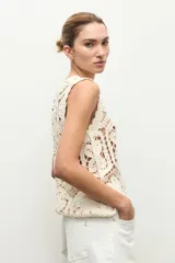Top sin mangas confeccionado en tejido de crochet con patrón geométrico y floral, en color beige claro.