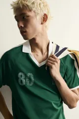 Polo de fútbol retro color verde oscuro, de corte regular fit, con cuello solapa blanco, mangas cortas con ribetes blancos y bandas en los hombros. Cuenta con estampado frontal del número 80 y un gráfico con efecto lavado.