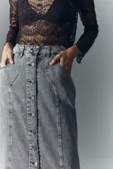 Falda midi de denim rígido con lavado gris, presenta cierre frontal con botones metálicos grabados y diseño de recortes verticales en el frente.