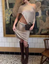Conjunto de dos piezas confeccionado en tejido metalizado plateado con brillo, compuesto por un top asimétrico de manga corta caída y una falda midi ajustada al cuerpo.