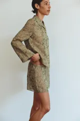 Camisa de cupro color verde militar con estampado jacquard de patrones florales y geométricos. Presenta cuello solapa, manga larga y cierre frontal con botones.