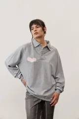 Buzo celeste de manga larga con cuello polo y cierre frontal de botones. Presenta un parche marrón bordado en el pecho.