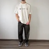 Remera oversize blanca de manga corta con detalles de líneas negras en las costuras de los hombros y mangas. Presenta un gran estampado en la espalda con el número 99 en diseño rayado y el logo de la marca en la parte superior.