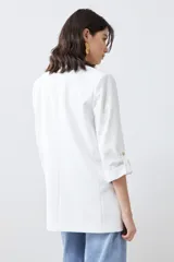 Blazer de corte recto y diseño minimalista, color blanco, con solapas clásicas, bolsillos frontales con solapa y mangas tres cuartos con detalle de botones.