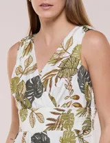 Vestido maxi sin mangas de base blanca con estampado de hojas tropicales en tonos verde y marrón. Presenta escote en V cruzado, cintura elastizada con paneles fruncidos y falda larga fluida con volados en el ruedo.