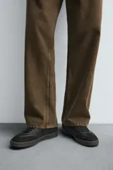 Zapatilla deportiva de estilo retro, color negro, con parte superior fabricada en combinación de piezas de cuero liso y gamuza perforada. Presenta una suela de goma en color marrón oscuro o ahumado en contraste.