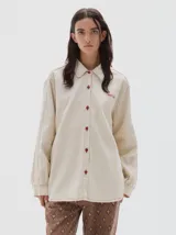 Camisa oversized de jean color crema, con botones rojos en forma de fresa y pespuntes a contratono. Tiene el logo "PASTICHE" bordado en rojo en el pecho.