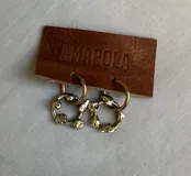 Aros colgantes formados por un pequeño aro superior de acero quirúrgico y un dije circular inferior de bronce con diseño orgánico y textura irregular.