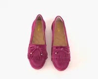 Mocasines de cuero gamuzado color fucsia, con flecos y un lazo con herrajes metálicos dorados en la capellada. Suela plana de goma.