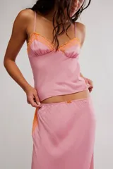 Conjunto de dos piezas de satén rosado, compuesto por una musculosa con tirantes finos y detalles de encaje naranja en el escote, y una falda larga al bies con volados y encaje naranja en el ruedo.