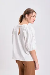 Remera color crudo con cuello redondo, mangas cortas abullonadas y pespuntes decorativos en color marrón claro.