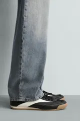Zapatilla de estilo retro con cordones, confeccionada en una combinación de piezas de cuero sintético negro y detalles en blanco, con suela dentada de goma en tono caramelo.