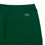 Pantalón de jogging verde oscuro con puños elásticos y cintura ajustable con cordón. Presenta bolsillos laterales y logo de Lacoste estampado en blanco en la pierna izquierda.