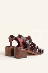 Sandalia plateada de cuero con tiras entrecruzadas, taco de madera y hebilla lateral.