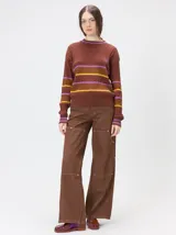 Sweater clásico de punto cable con cuello redondo a la base, mangas largas y fit al cuerpo. De color marrón con franjas horizontales violetas y amarillas, cuenta con el cuello, puños y ruedo acanalados, además de un pequeño logo bordado en el pecho.