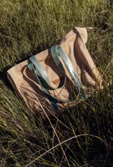 Bolso tipo tote bag de lona color beige, con asas de cuero verde.