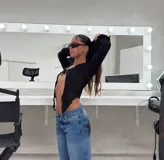 Top negro de tejido texturizado, manga larga acampanada y escote pronunciado que se ata con un nudo central, dejando el abdomen al descubierto.