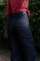 Jean de corte wide leg y tiro alto, confeccionado en denim de color azul oscuro. Presenta costuras decorativas visibles en los laterales y un diseño de pierna amplia.