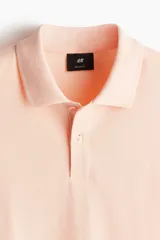 Remera polo color salmón de piqué de algodón, corte regular fit, con cuello clásico, tapeta de dos botones, mangas cortas y terminaciones acanaladas en cuello y mangas.