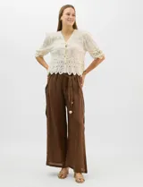 Blusa de algodón semitransparente con diseño floral bordado a tono. Presenta escote en V, cierre frontal con botones y mangas al codo ligeramente abullonadas. Incluye detalles de encaje calado estilo macramé en los puños y en el ruedo con terminaciones en ondas.