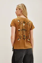 Remera de algodón color marrón mostaza con estampado en la espalda de un ojo místico rodeado de fases lunares, estrellas y motivos florales en color negro.