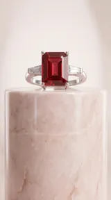 Anillo de plata con piedra central rectangular de color rojo intenso y piedras laterales tipo baguette.