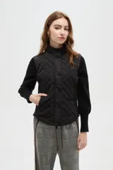 Chaleco negro con diseño capitoneado, cierre frontal con botones a presión y cuello alto.