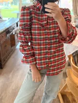 Camisa de manga larga con estampado de cuadros en tonos rojos, blancos y azules. Presenta un diseño con mangas abullonadas divididas por secciones elásticas y cierre frontal con botones.
