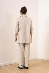 Blazer de cuero sintético color beige, con diseño de doble botonadura, solapas clásicas y bolsillos frontales con solapa.