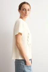 Remera color natural de manga corta, con cuello redondo y un aplique cuadrado de crochet con diseño floral en el centro del pecho.