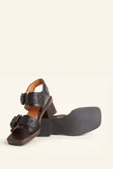 Sandalias de cuero negro con taco bloque de madera tallada, tiras con hebillas grandes y punta cuadrada.