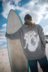 Hoodie gris con capucha y cordones ajustables, de corte holgado y puños elásticos. Estampado en la espalda con una sirena, una flor de hibisco y la frase "Glass Waves".