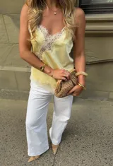 Blusa de satén color amarillo suave, estilo camisola, con delicados detalles de encaje blanco en el escote y el dobladillo, breteles finos y silueta fluida.