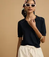 Blusa negra de punto con cuello polo, escote en V y mangas cortas. Detalle de mini perlas aplicadas en el cuello.