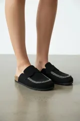 Zueco destalonado de color negro, con costuras decorativas blancas alrededor de la puntera, tira en el empeine y suela estilo corcho.