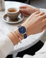 Reloj analógico con caja redonda de metal en tono oro rosa y esfera azul con efecto brillante. Cuenta con una malla de cuero en color azul oscuro y movimiento de cuarzo japonés.