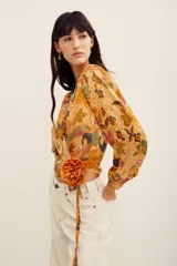 Camisa tipo cruzada (wrap) de manga larga con estampado floral multicolor en tonos mostaza y bordó. Cuenta con escote en V cruzado y detalle de lazo lateral con flor aplicada.