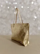 Bolso shopper de cuero color dorado con textura crocco, asas de hombro en tono semi natural y cierre superior. Cuenta con diseño espacioso, bolsillo interior y detalle artístico exclusivo de la marca.