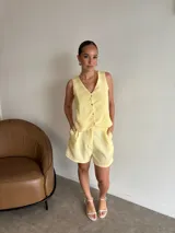 Conjunto de dos piezas color negro, compuesto por un chaleco con escote en V y botones al frente, y un short tipo bermuda con bolsillos laterales.